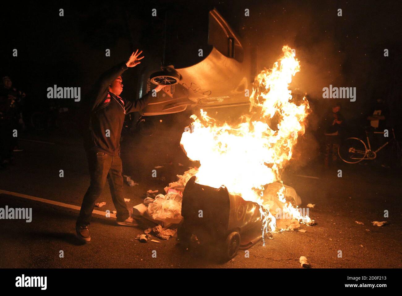 A protester throws a trash can on a fire during a demonstration in Oakland, California following the grand jury decision in the shooting of Michael Brown in Ferguson, Missouri November 24, 2014. Protests were also staged in New York, Chicago, Washington, D.C. and Seattle over the case that has highlighted long-standing racial tensions not just in predominantly black Ferguson but across the United States. REUTERS/Elijah Nouvelage (UNITED STATES - Tags: CIVIL UNREST) Stock Photo