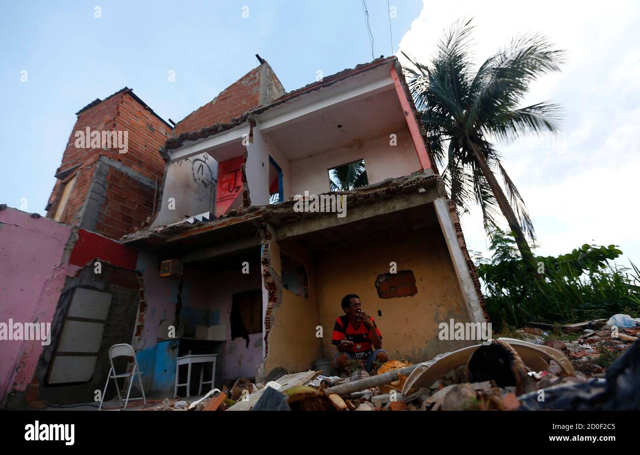 Luis Geraldo, 52, smokes a cigarette in his house where the co-owners have left and their part of the building demolished, at the Vila Autodromo favela in Rio de Janeiro January 28, 2015. Street addresses jump in the Vila Autodromo favela: 39, 42, 48, 51. The missing numbers belonged to homes now reduced to rubble to make way for the Olympic Park in Rio de Janeiro. But 18 months before the Olympic Games begin, about 50 families still refuse to leave, clinging on despite increasing isolation and irregular access to basic services like water and electricity. The land conflict in Vila Autodromo, Stock Photo