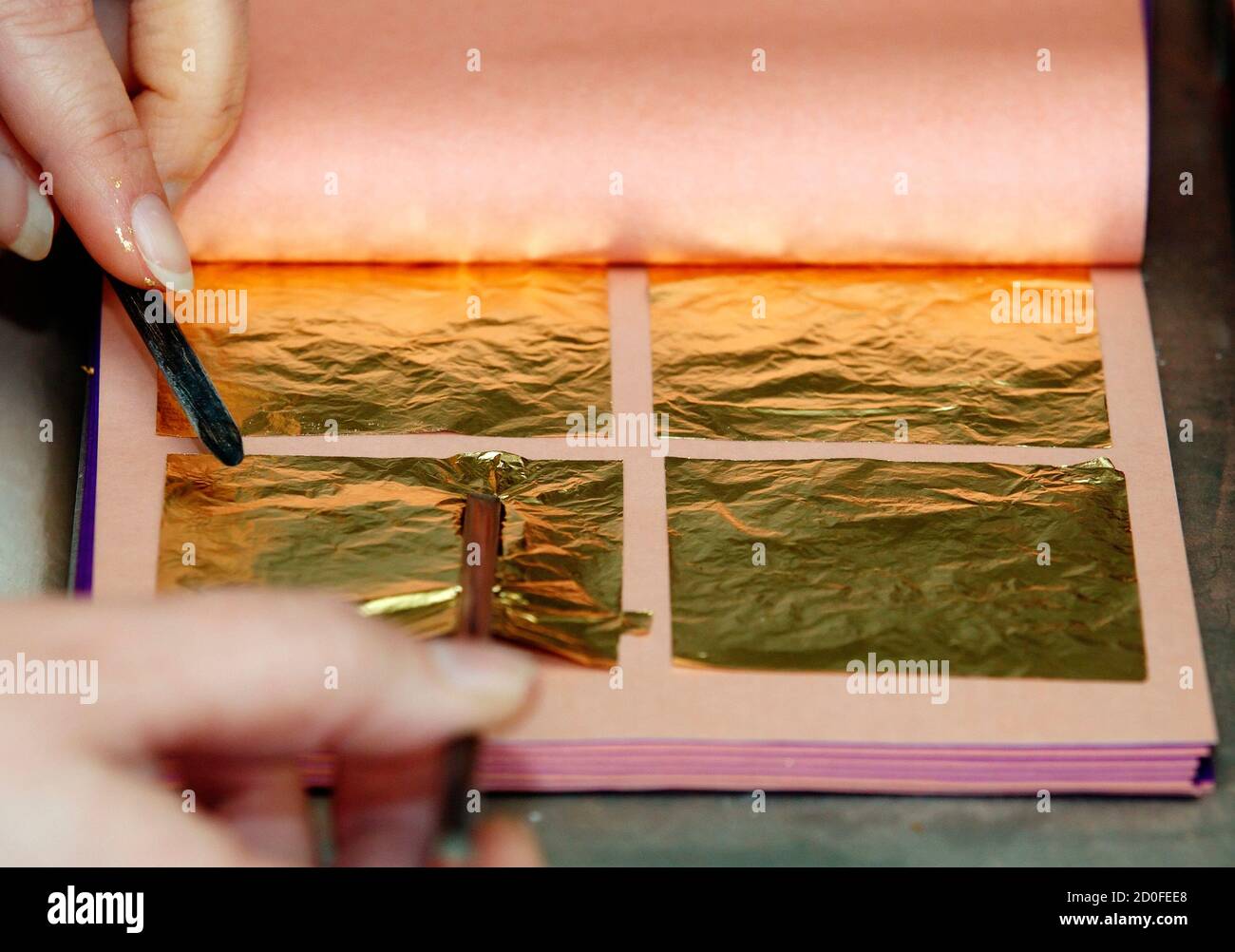 A worker places sheets of finished gold leaf between tissue paper at Erich  Dungl's gold leaf workshop in Schwechat March 4, 2014. Each handmade sheet  of gold leaf is produced by squeezing