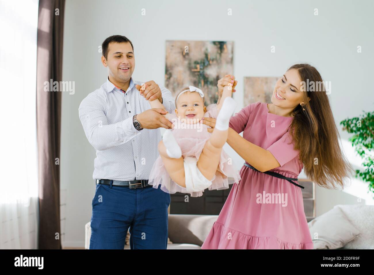 Happy young parents swing their daughter in their arms, toss it up. Happy family time Stock