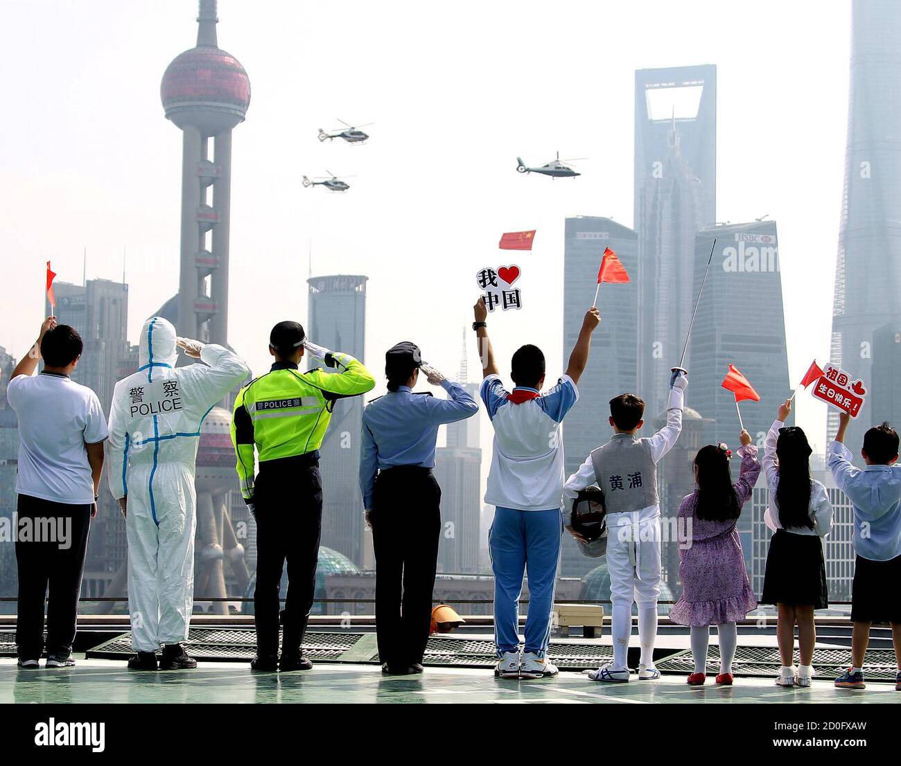 Beijing, China. 1st Oct, 2020. People salute as helicopters with Chinese national flag flies over the Huangpu River to celebrate the 71st anniversary of the founding of the People's Republic of China in Shanghai, east China, Oct. 1, 2020. Credit: Chen Fei/Xinhua/Alamy Live News Stock Photo