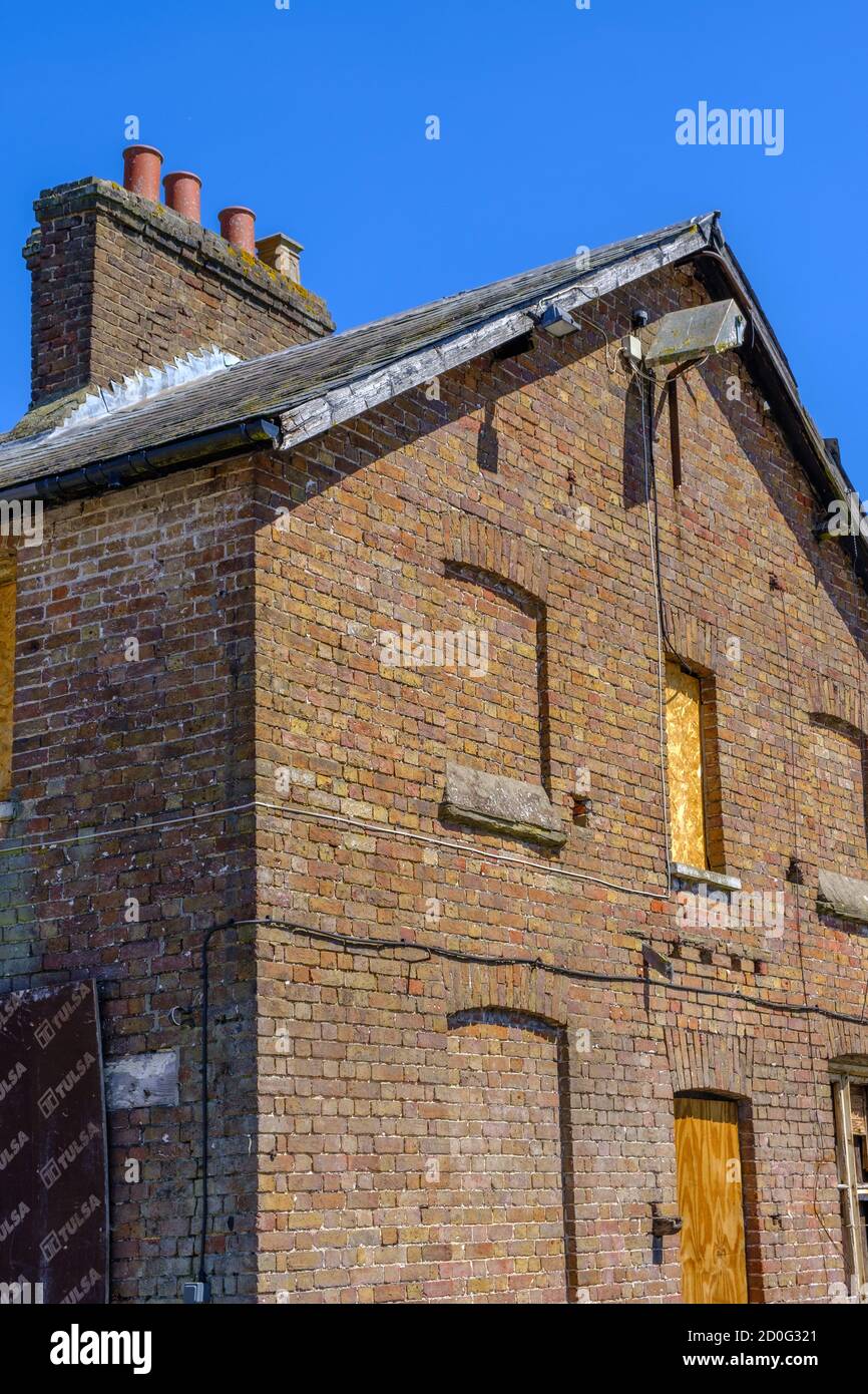 Deserted brick building with bricked up windows, boarded up window & doorway & Victorian brick chimney stack with pots. Blue sky. Pinner Park Farm. Stock Photo