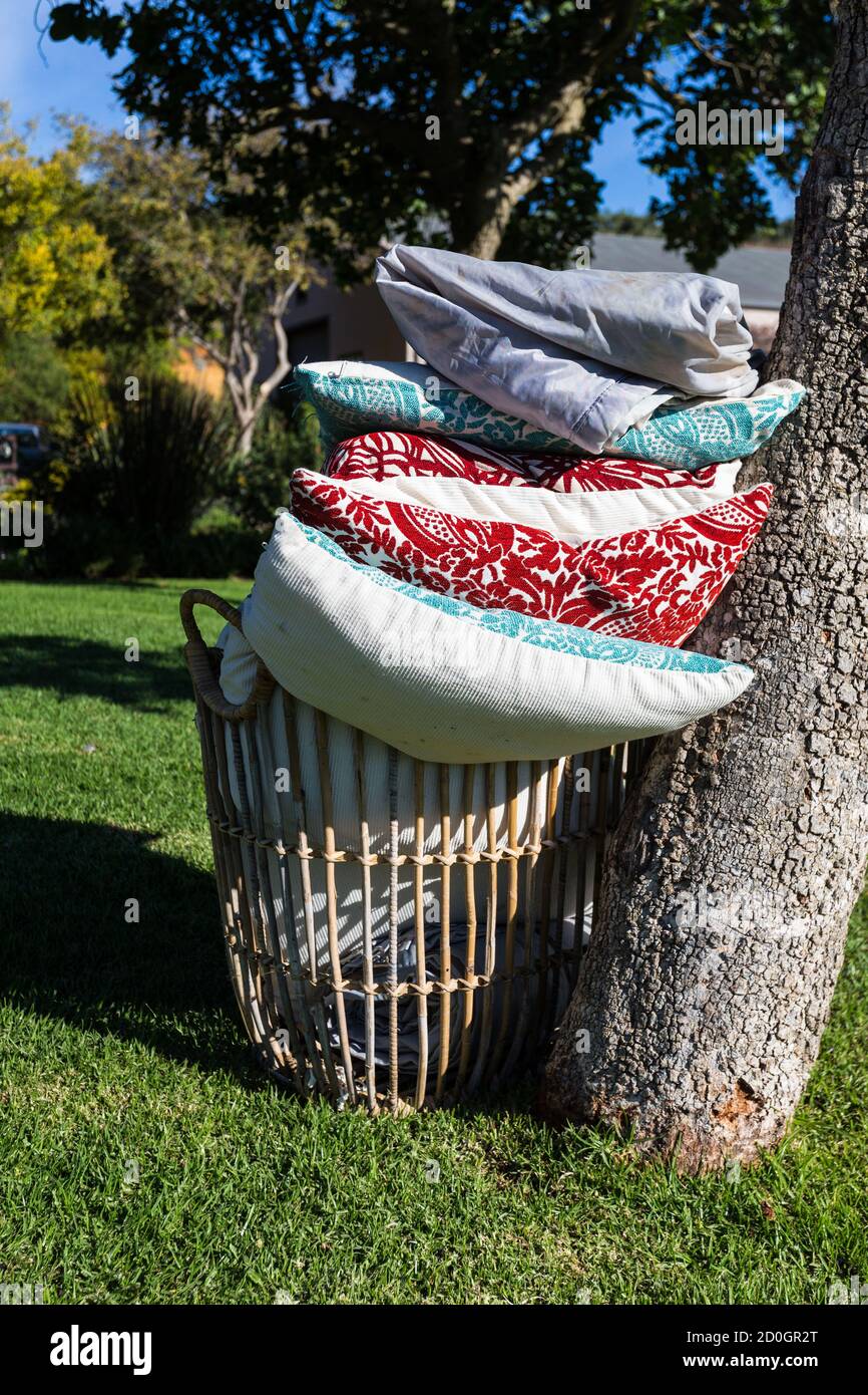 basket filled with colourful cushions and blankets or rugs on the grass under a tree concept picnic in the park on the lawn Stock Photo