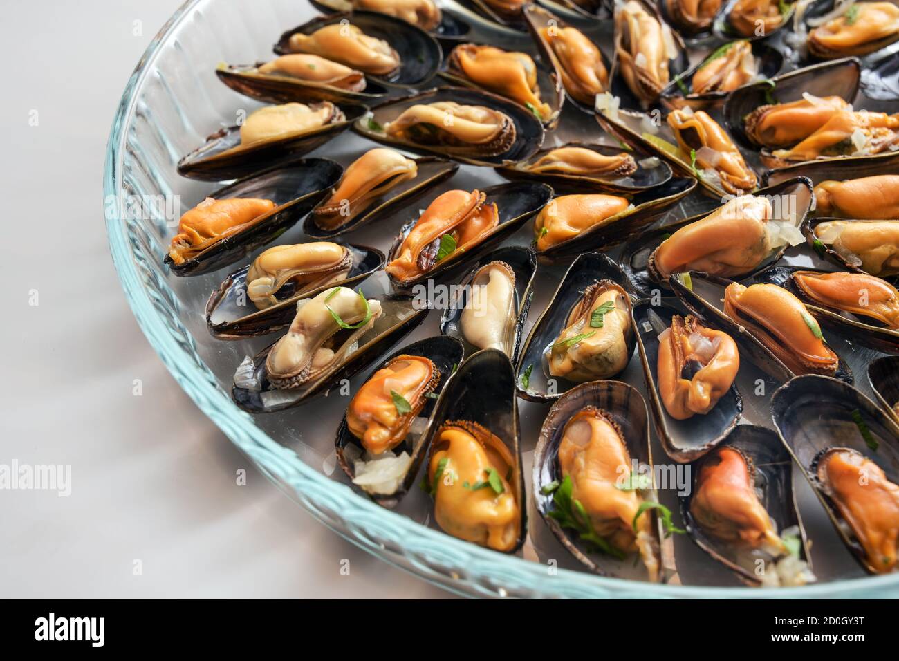 Freshly cooked blue mussels with onion and herbs served on a large glass plate, selected focus, very narrow depth of field Stock Photo