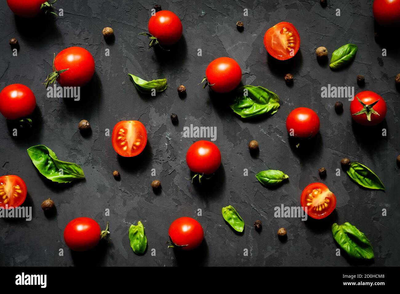 Halved Juicy Cherry Tomatoes and Basil Leaves on a black background ...