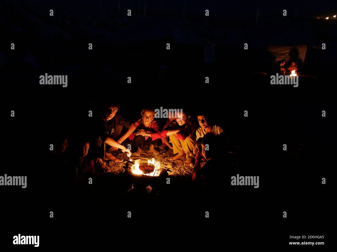 Children from the minority Yazidi sect, who fled violence in the Iraqi town of Sinjar, wait for food by a fire in Bajed Kadal refugee camp, southwest of Dohuk province August 22, 2014. REUTERS/Youssef Boudlal (IRAQ - Tags: CIVIL UNREST POLITICS CONFLICT TPX IMAGES OF THE DAY FOOD SOCIETY) Stock Photo