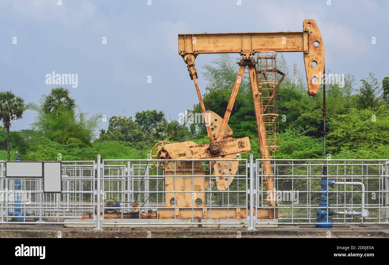 Old rusty oil pump jack extracting crude oil and natural gas from an oil well in green oil field background Stock Photo