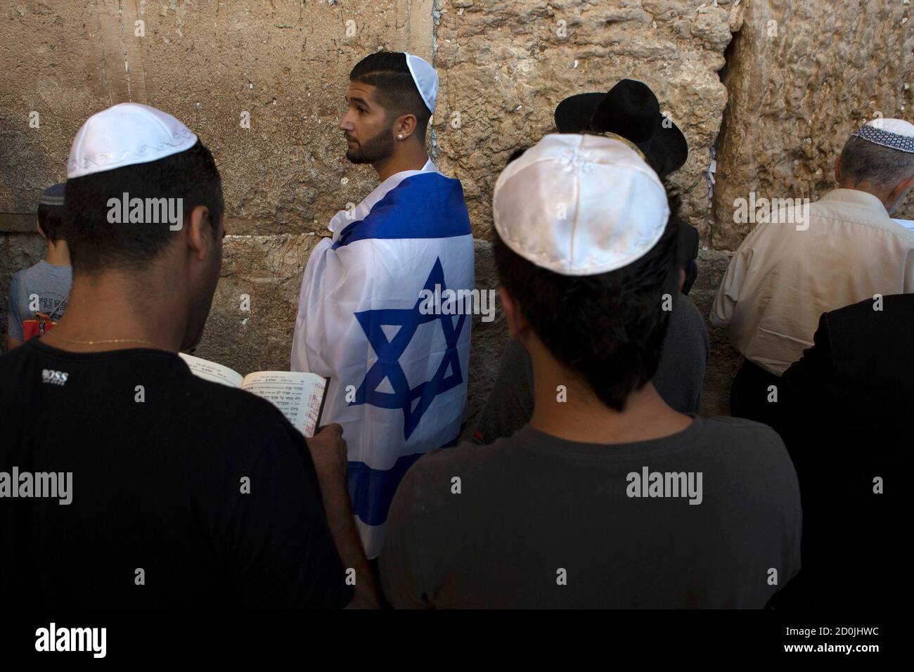 A Jewish worshipper, wrapped in an Israeli flag, attends a special prayer at the Western Wall in Jerusalem's Old City for the well-being of Israeli soldiers in Gaza July 23, 2014. Gaza fighting raged on Wednesday, displacing thousands more Palestinians in the battered territory as U.S. Secretary of State John Kerry said efforts to secure a truce between Israel and Hamas had made some progress. Israel announced that three of its soldiers were killed by explosive devices on Wednesday, lifting the army death toll to 32.  REUTERS/Siegfried Modola (JERUSALEM - Tags: RELIGION CIVIL UNREST CONFLICT) Stock Photo