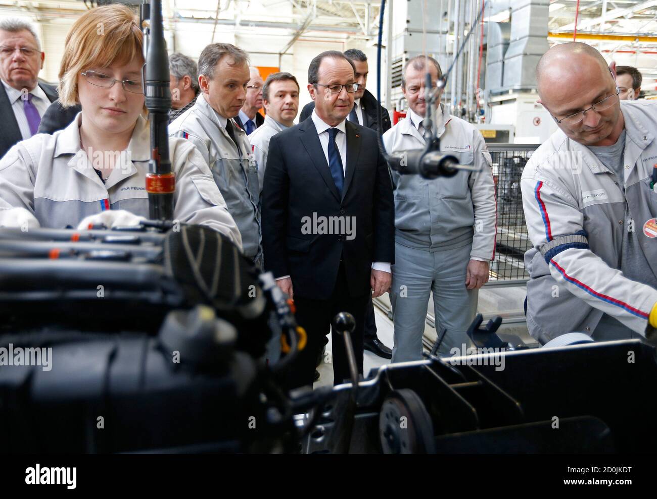 French President Francois Hollande (L) looks at workers as he visits the engines assembly line at the French carmaker PSA Peugeot Citroen engine factory in Tremery near Metz, North Eastern France, March 27, 2015. PSA Peugeot Citroen said on Friday it had chosen a French factory over a rival Spanish plant to expand engine production. The troubled carmaker said it will upgrade the Tremery site to produce the turbo version of a staple three-cylinder engine already manufactured there, safeguarding local jobs. REUTERS/Vincent Kessler Stock Photo
