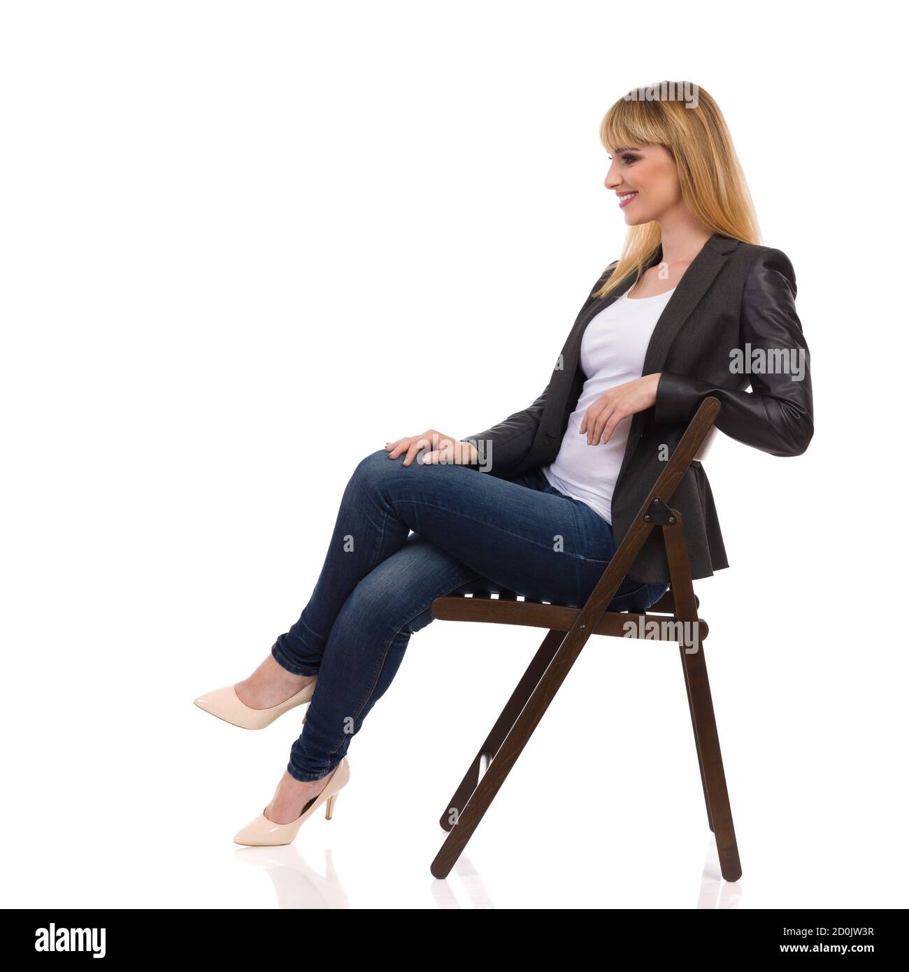 Smiling beautiful young businesswoman is sitting on a chair and looking away. Side view. Full length studio shot isolated on white. Stock Photo