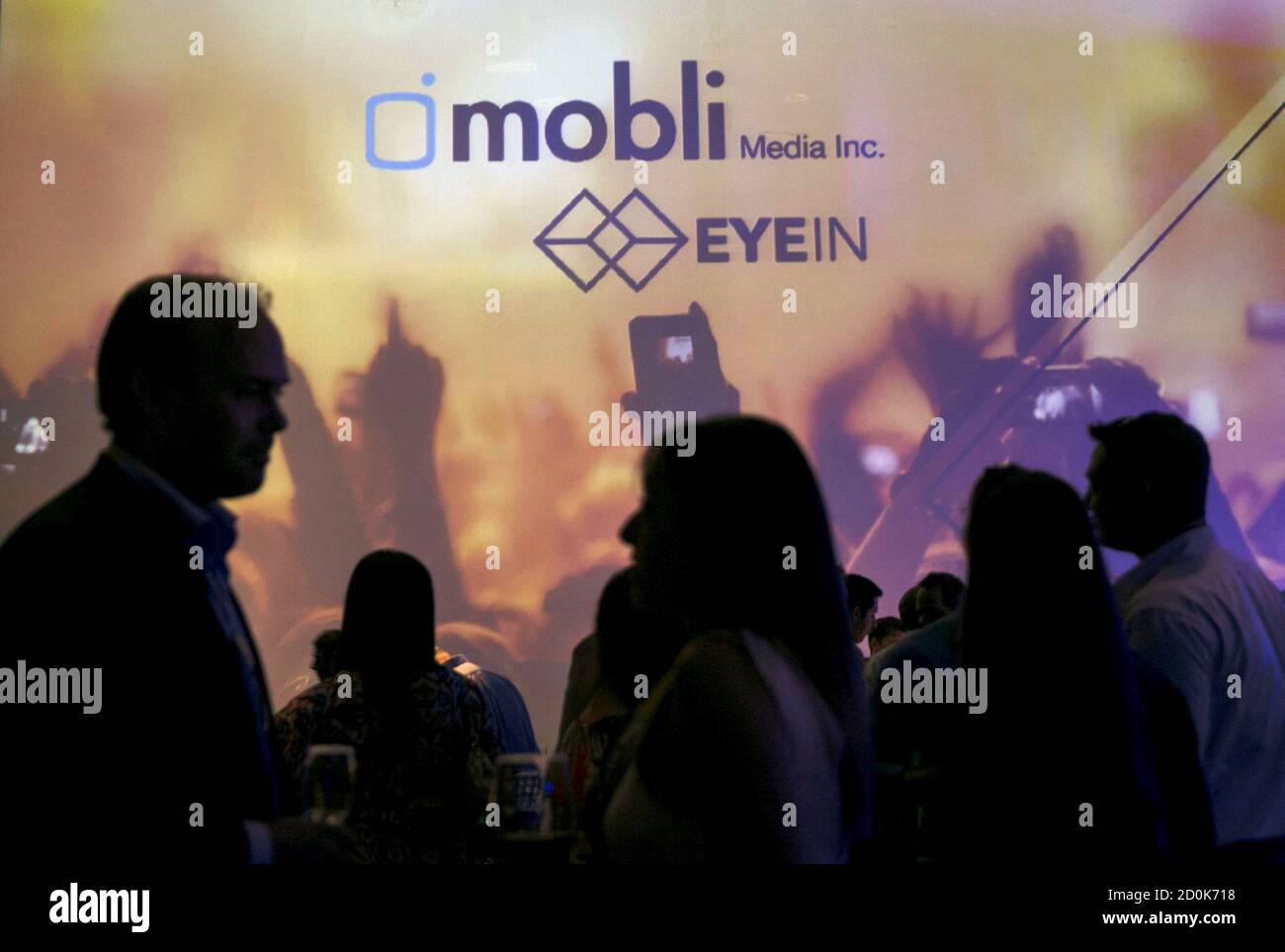 People are silhouetted in front of a screen depicting the logo of Israeli start-up, Mobli Media Inc, during their launch in Tel Aviv, Israel June 15, 2015. Israeli start-up Mobli Media Inc is taking on Internet giants Google, Facebook and Yahoo with an innovative online search tool to find the latest photos and videos across social media sites, the company said on Monday. REUTERS/Baz Ratner Stock Photo