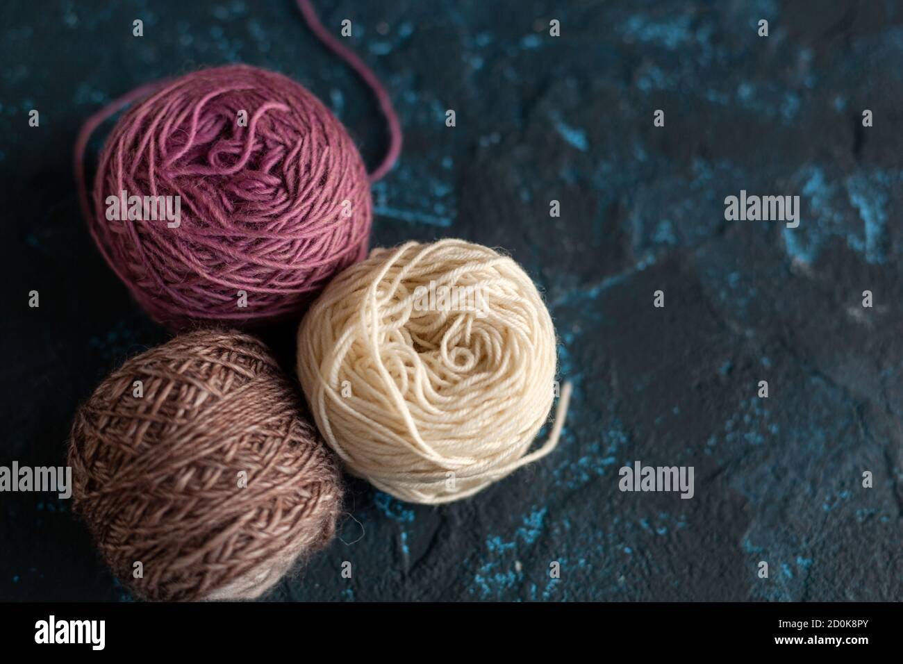 three beige pink brown Color balls skein of wool yarn for crochet and knit on dark blue texture putty concrete. Flatlay image with space for text. Stock Photo