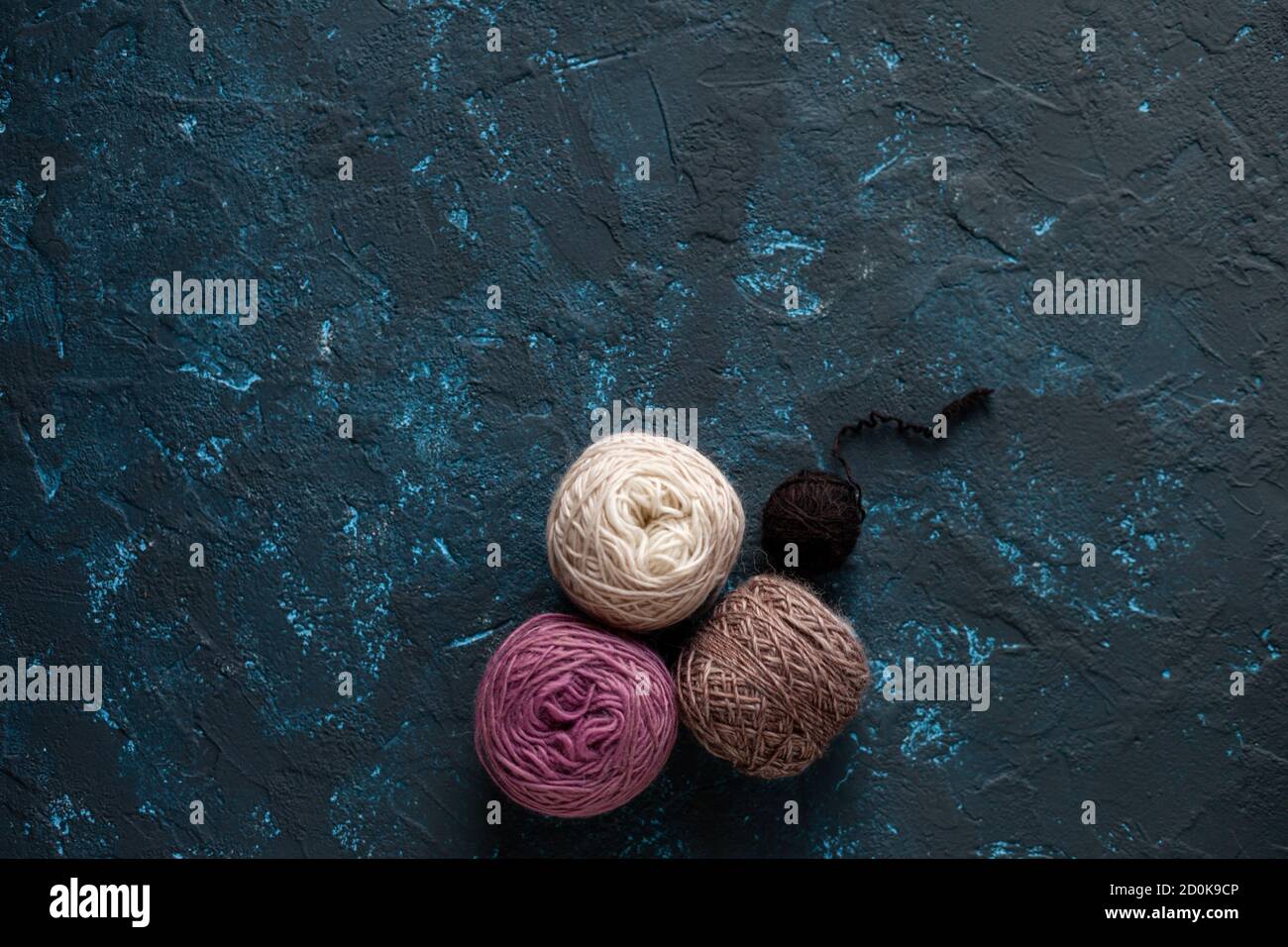Four beige pink brown Color balls skein of wool yarn for crochet and knit on dark blue texture putty concrete. Flatlay image with space for text. Stock Photo