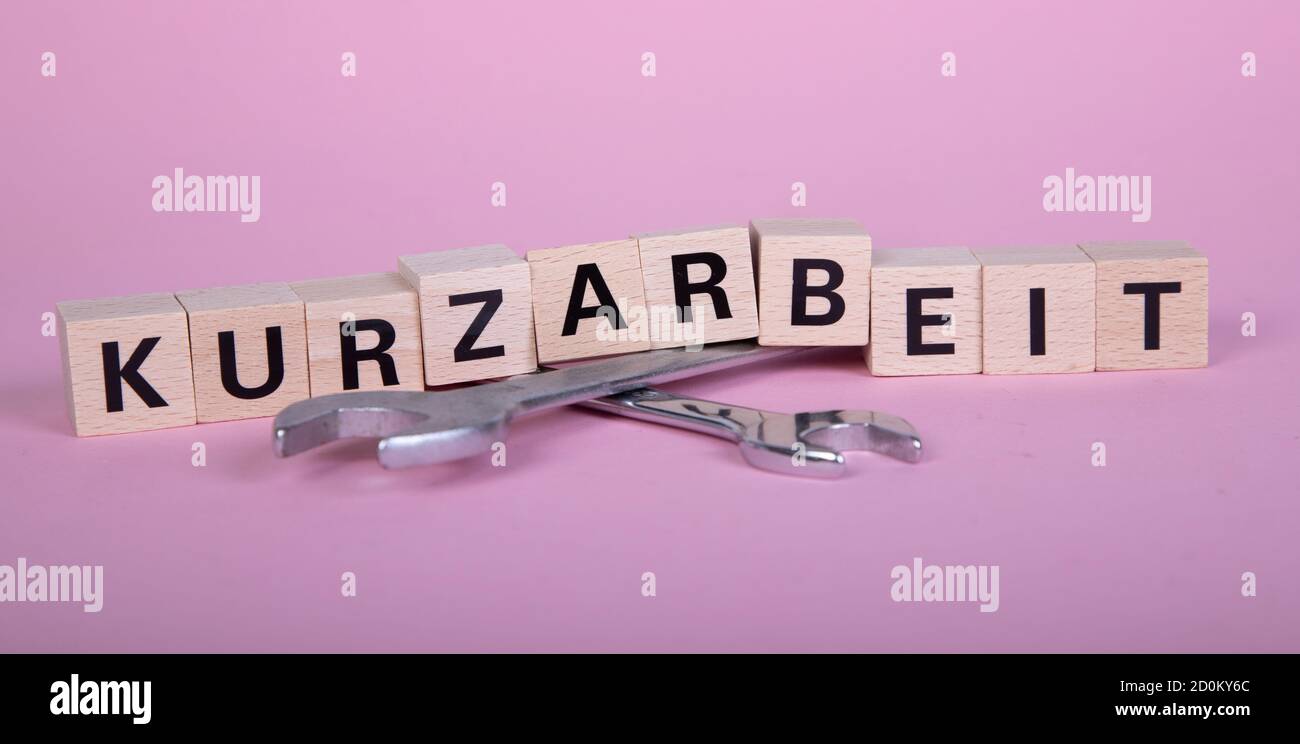 wooden blocks with german word for short time work, Kurzarbeit, above of two wrenches, pink background Stock Photo