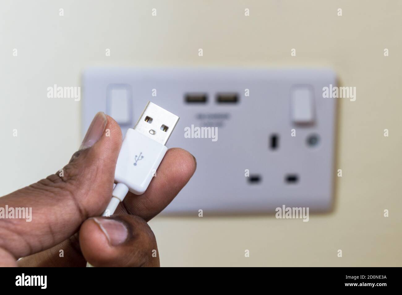 Man holding USB plug pin in front of two gang uk socket with USB ports Stock Photo