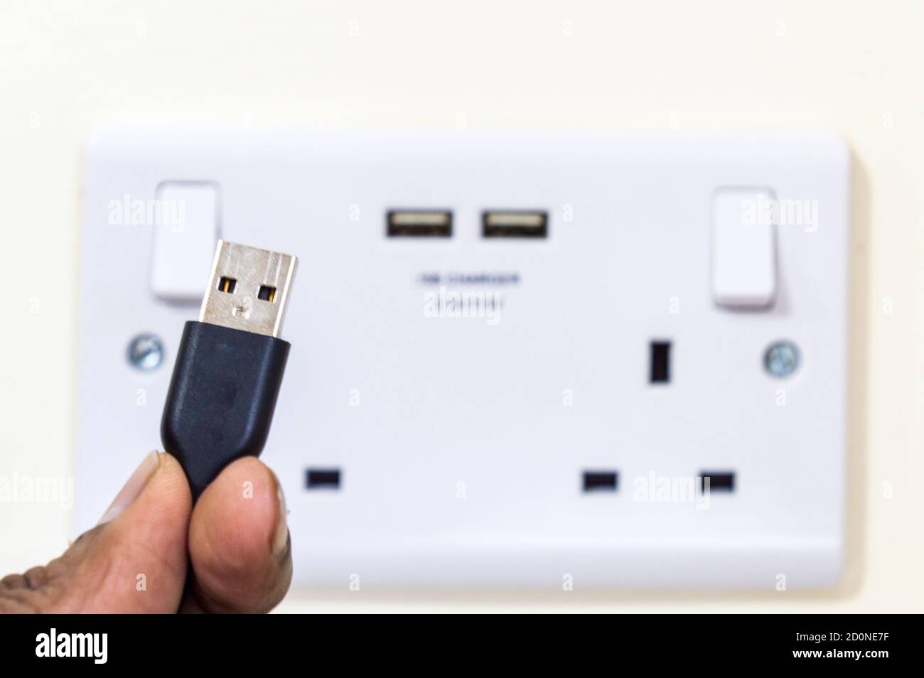 Man holding USB plug pin in front of two gang uk socket with USB ports Stock Photo