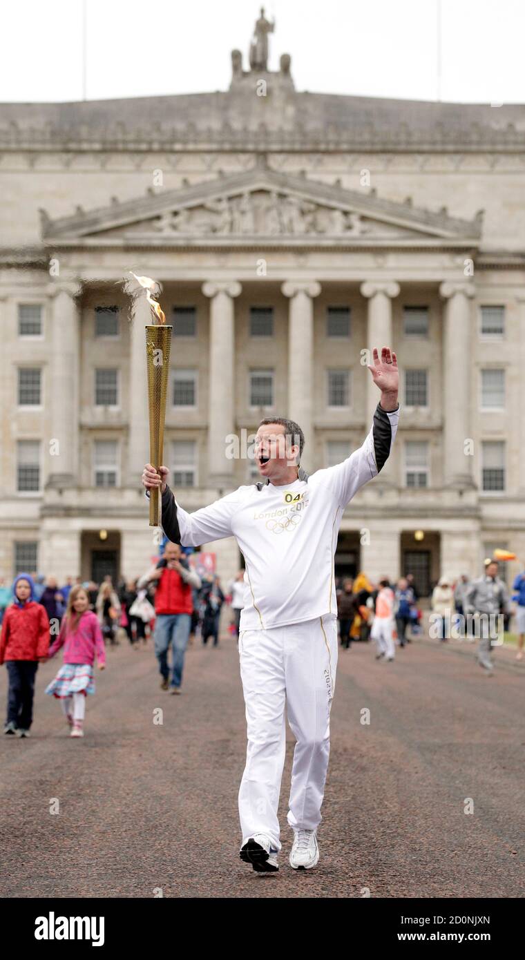 John Mcalpine carries the Olympic torch in front of Parliament Buildings in Belfast June 3, 2012. On Sunday the Olympic flame - on a five-day visit to Northern Ireland - will be carried to the Titanic Building, recently opened in Belfast's docklands to commemorate the famous liner which was built in the city and sank 100 years ago. It will then make its way through more than 60 towns and villages across Northern Ireland, carried by about 600 local people aged between 12 to 93. REUTERS/Cathal McNaughton  (NORTHERN IRELAND - Tags: SPORT OLYMPICS SOCIETY) Stock Photo