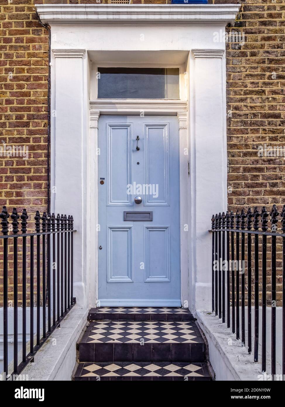 A classic London house with light blue-grey doors in Notting Hill. With a white frame against the dark brown brick wall and the chess board pavement. Stock Photo