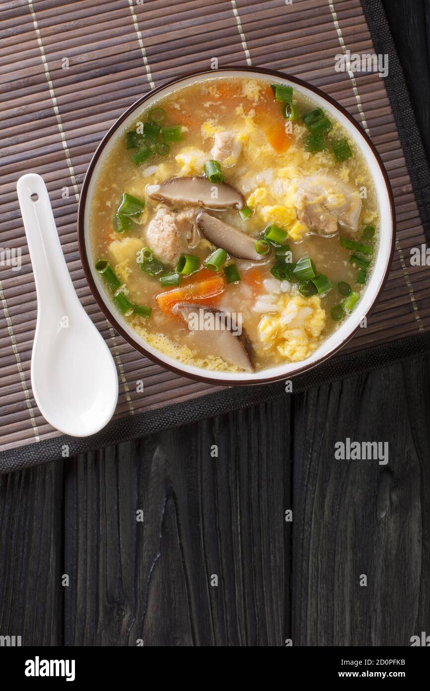 Japanese Zosui rice soup with egg, mushrooms, vegetables and chicken meat close-up in a bowl on the table. Vertical top view from above Stock Photo