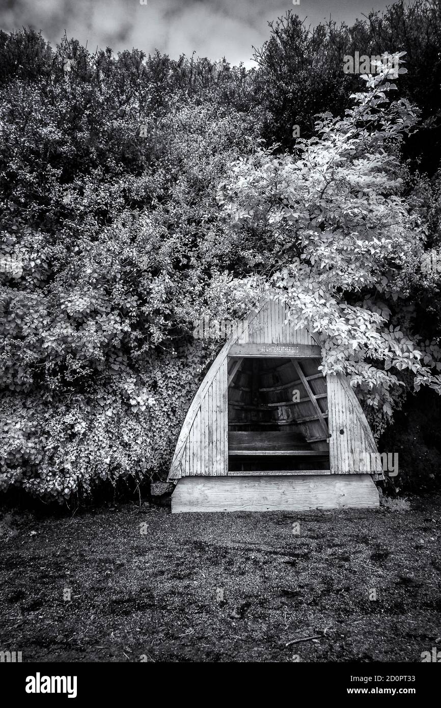 An infra red image of a shelter made out of the bow of a small wooden boat on the The Gannel at low tide in Newquay in Cornwall. Stock Photo