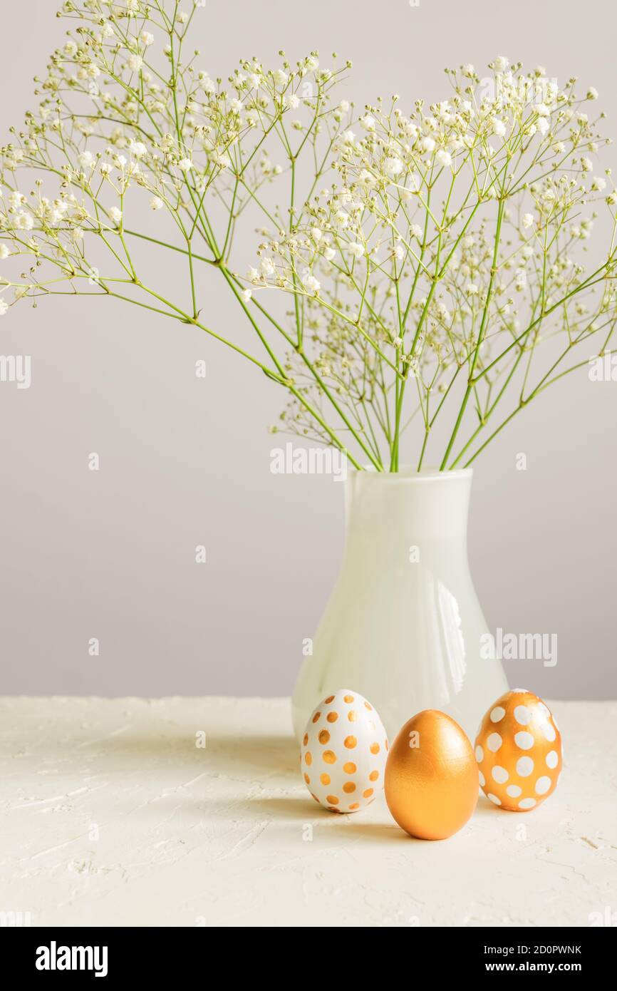 Easter golden eggs and bouquet of gypsophila flowers on the gray wall ...