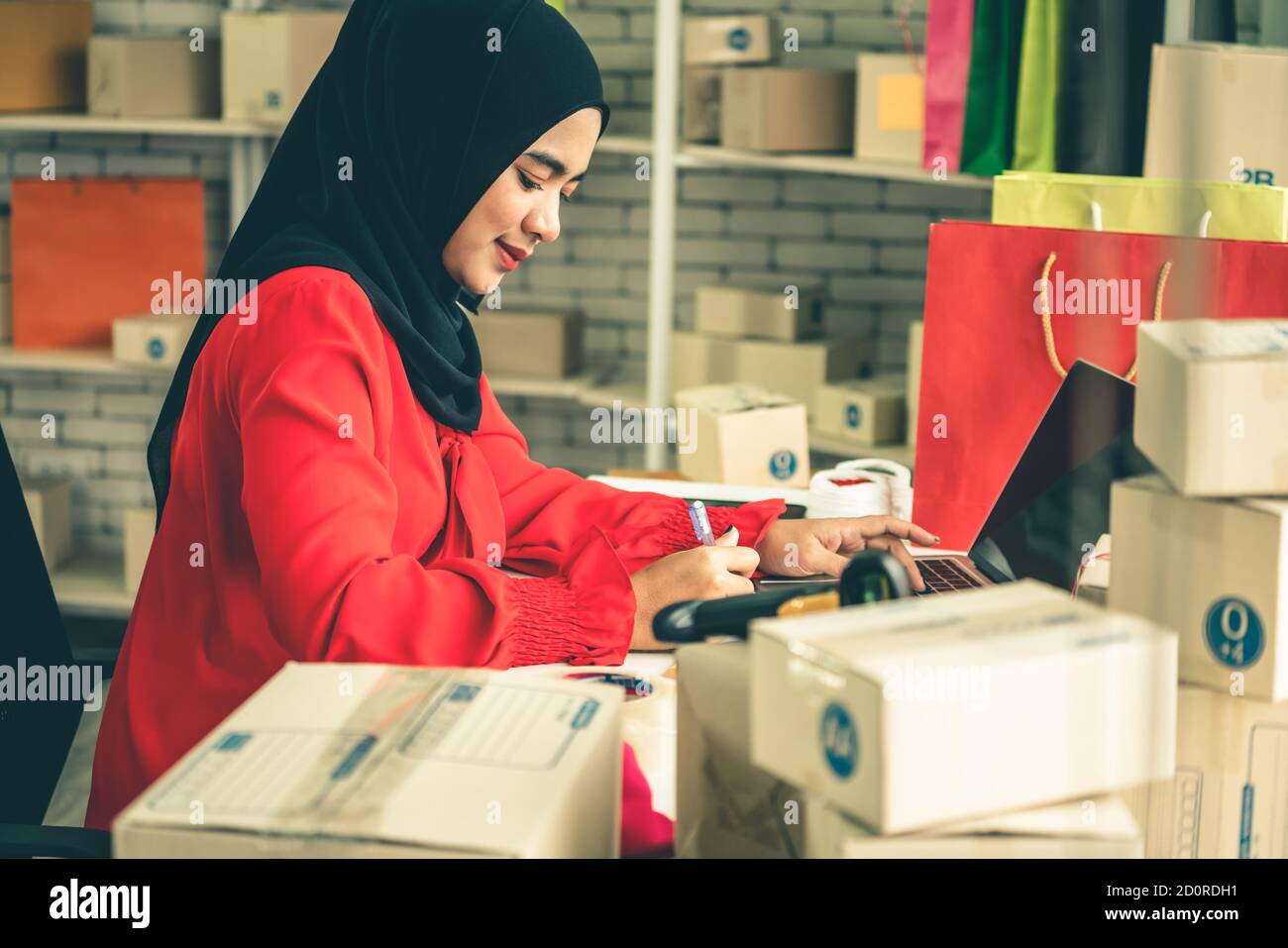 Muslim online seller at home office with shipping box for delivery to customer. Small business owner or entrepreneur doing e-commerce business on the Stock Photo