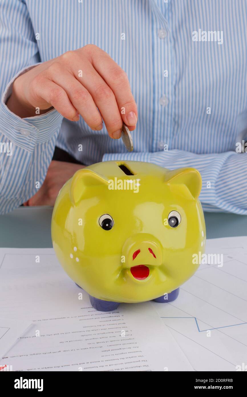 Female hand putting coin into piggy bank Stock Photo - Alamy