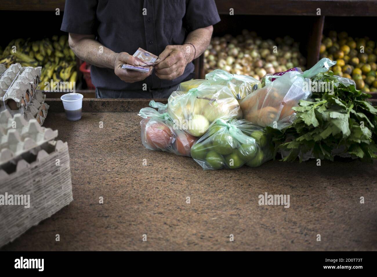 A clerk counts Venezuelan bolivar banknotes after selling goods to a customer at a fruit and vegetable store in Caracas, July 10, 2015. A debilitating recession and a drop in oil prices have harmed the OPEC nation's ability to provide dollars through its complex three-tiered currency control system, pushing up the black market rate at a dizzying speed. The bolivar sank past 600 per U.S. dollar on Thursday, compared with 73 a year ago, according to anti-government website DolarToday. REUTERS/Marco Bello Stock Photo
