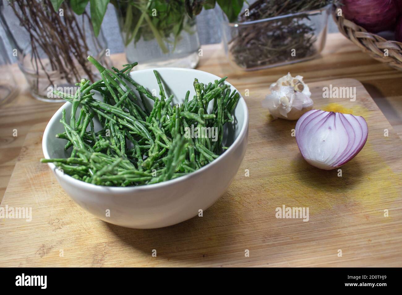 A bowl full of glasswort (sea asparagus) on a wooden cutting board with some herbs in the background Stock Photo