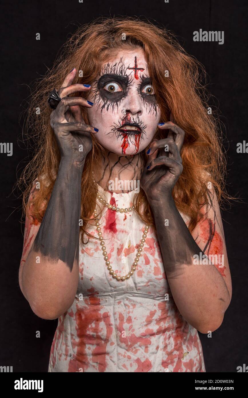 A young woman with red hair and professional make-up to look creepy, wearing bloody white clothes. Halloween concept Stock Photo