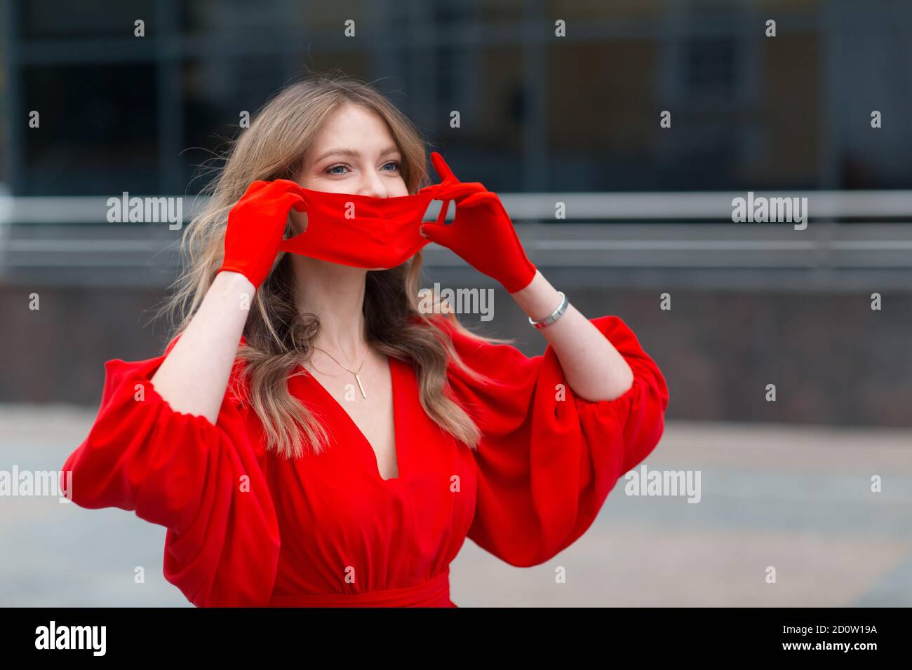 Young woman in red dress and gloves puts on medical protective face ...