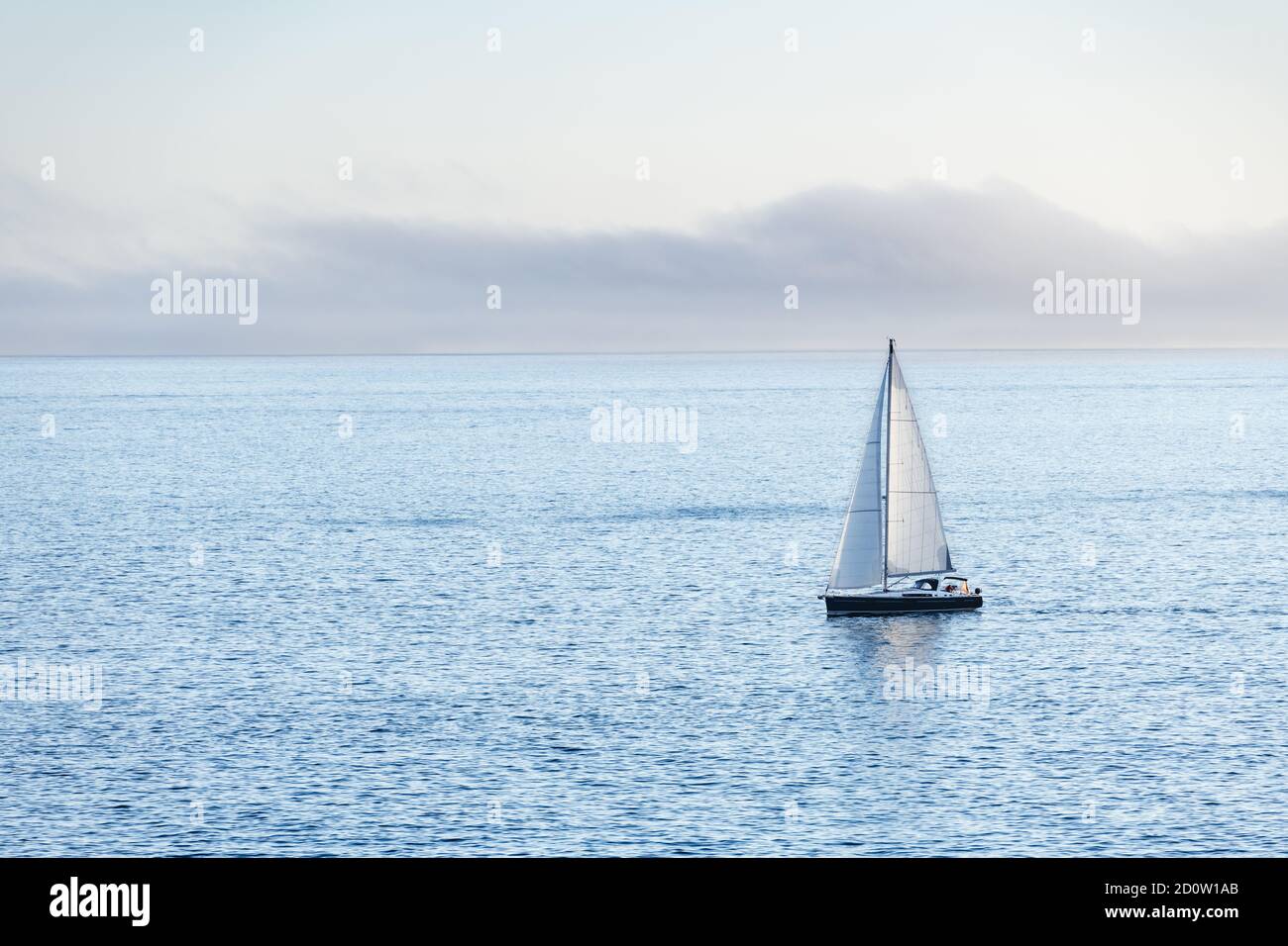 A lonely boat sails away from Ons Island in the Ria de Pontevedra in Galicia at dusk. Stock Photo