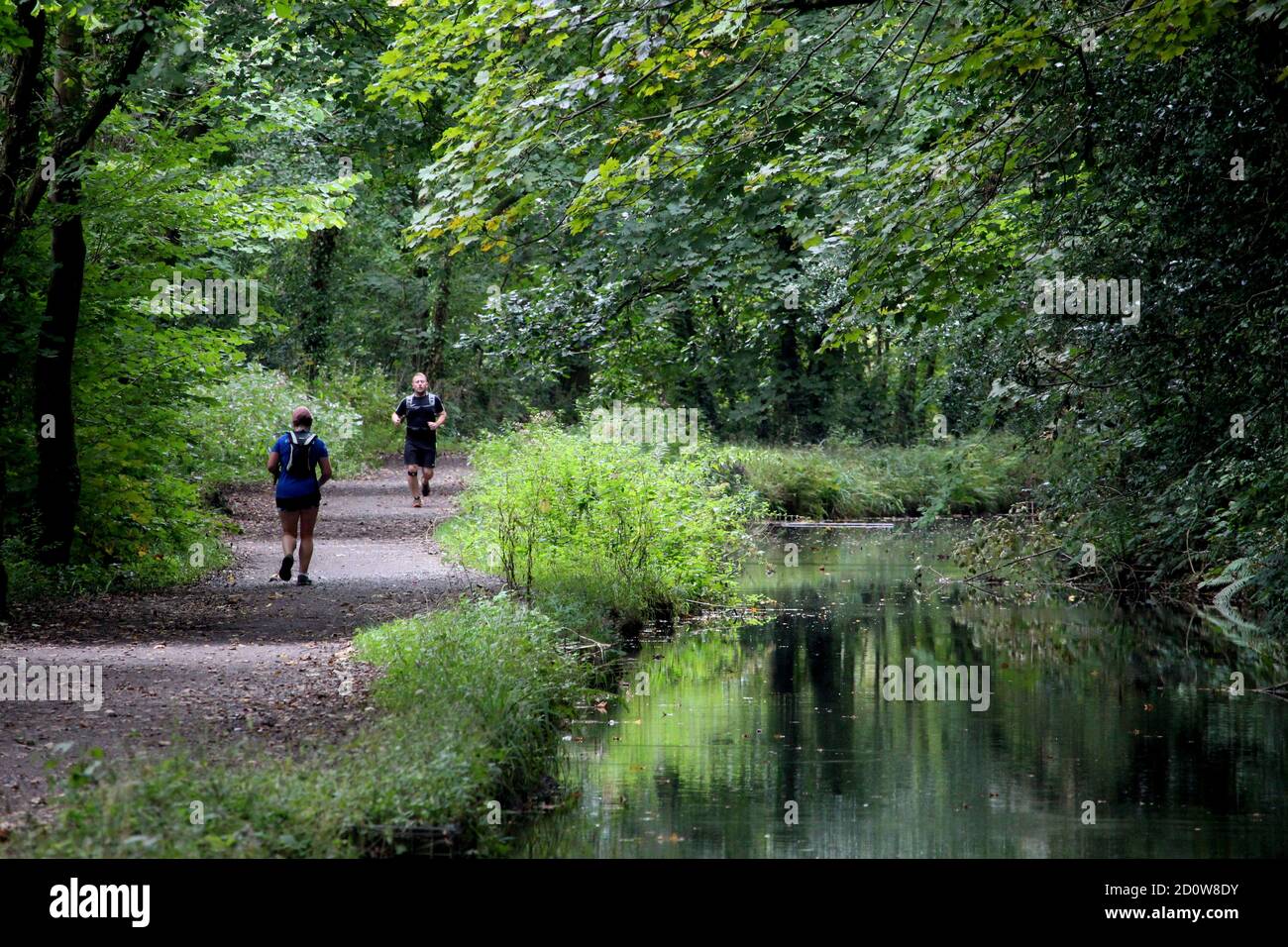 Two male runners take exercise alongside a still and calm river Stock Photo