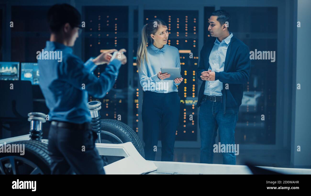 Automotive Design Engineer and Scientist with Tablet Discuss the Electric Car Chassis Prototype. In Innovation Laboratory Facility Concept Vehicle Stock Photo