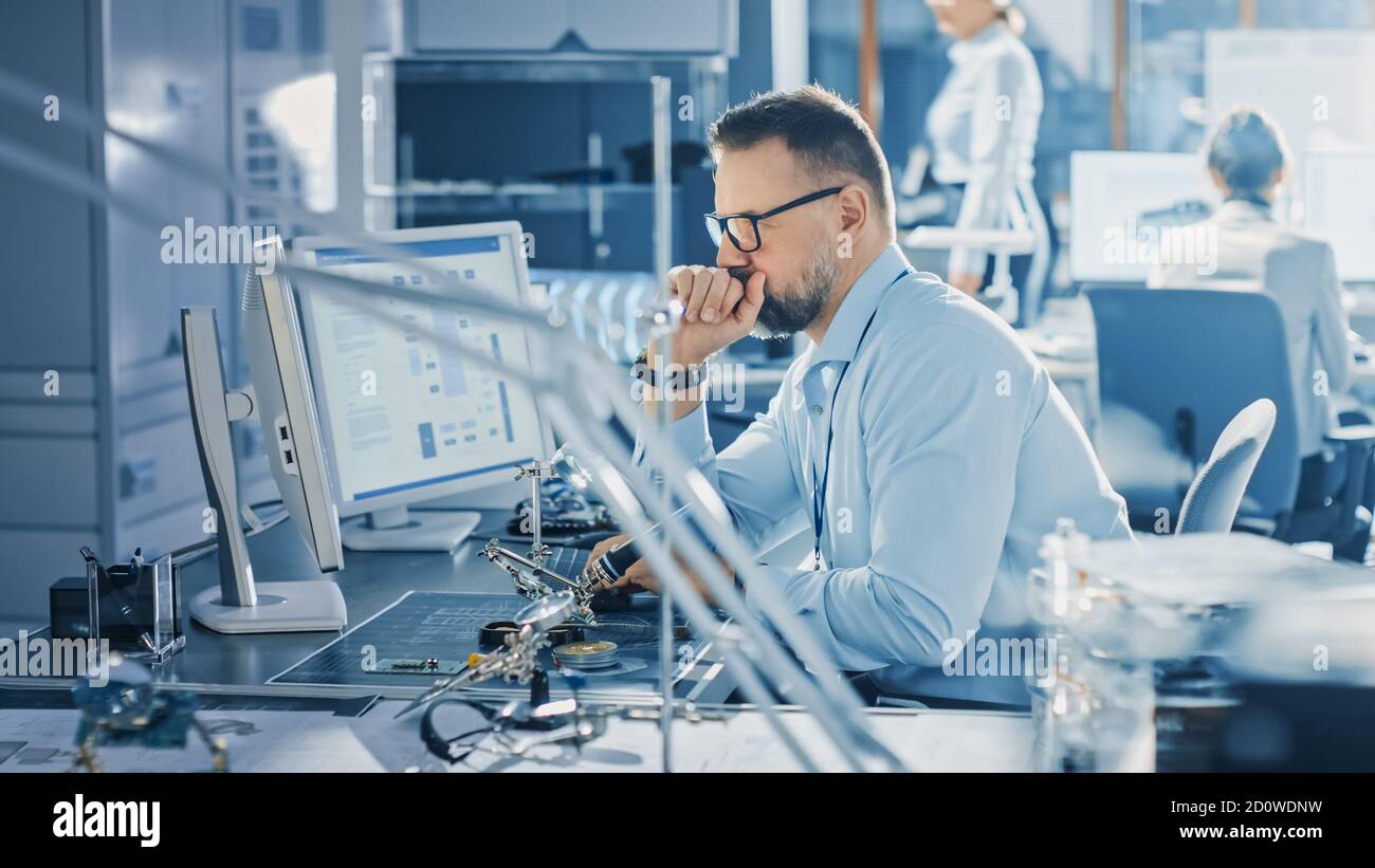 Electronics Development Engineer Working on Computer, Designing Motherboard, Doing Maintenance of Devices and Soldering Circuit Boards. Professionals Stock Photo