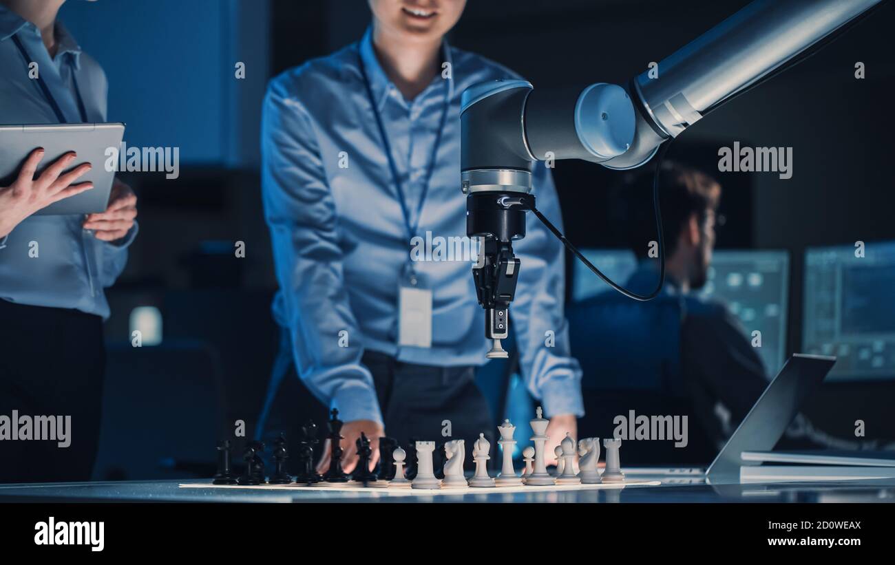 Two Development Engineers are Discussing and Testing an Artificial Intelligence Interface by Playing Chess with a Futuristic Robotic Arm. They are in Stock Photo
