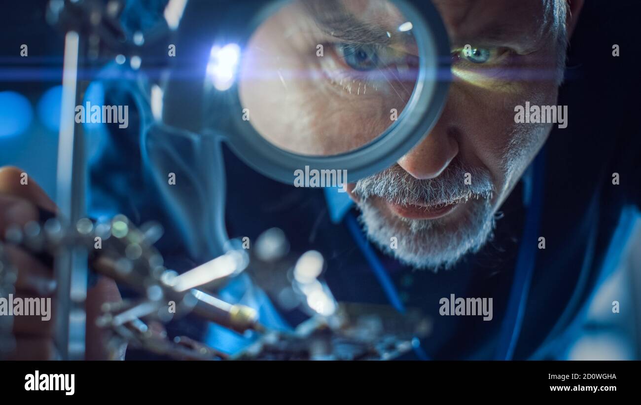 Electronics Maintenance and Repair Engineer Soldering Motherboard, Microchip and Circuit Board, Looking through Magnifying Glass. Conceptual Shot Stock Photo
