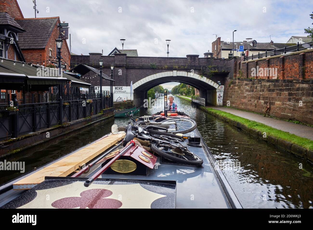 A woman steers a narrowboat under a bridge on the Bridgewater Canal at Sale, Manchester Stock Photo