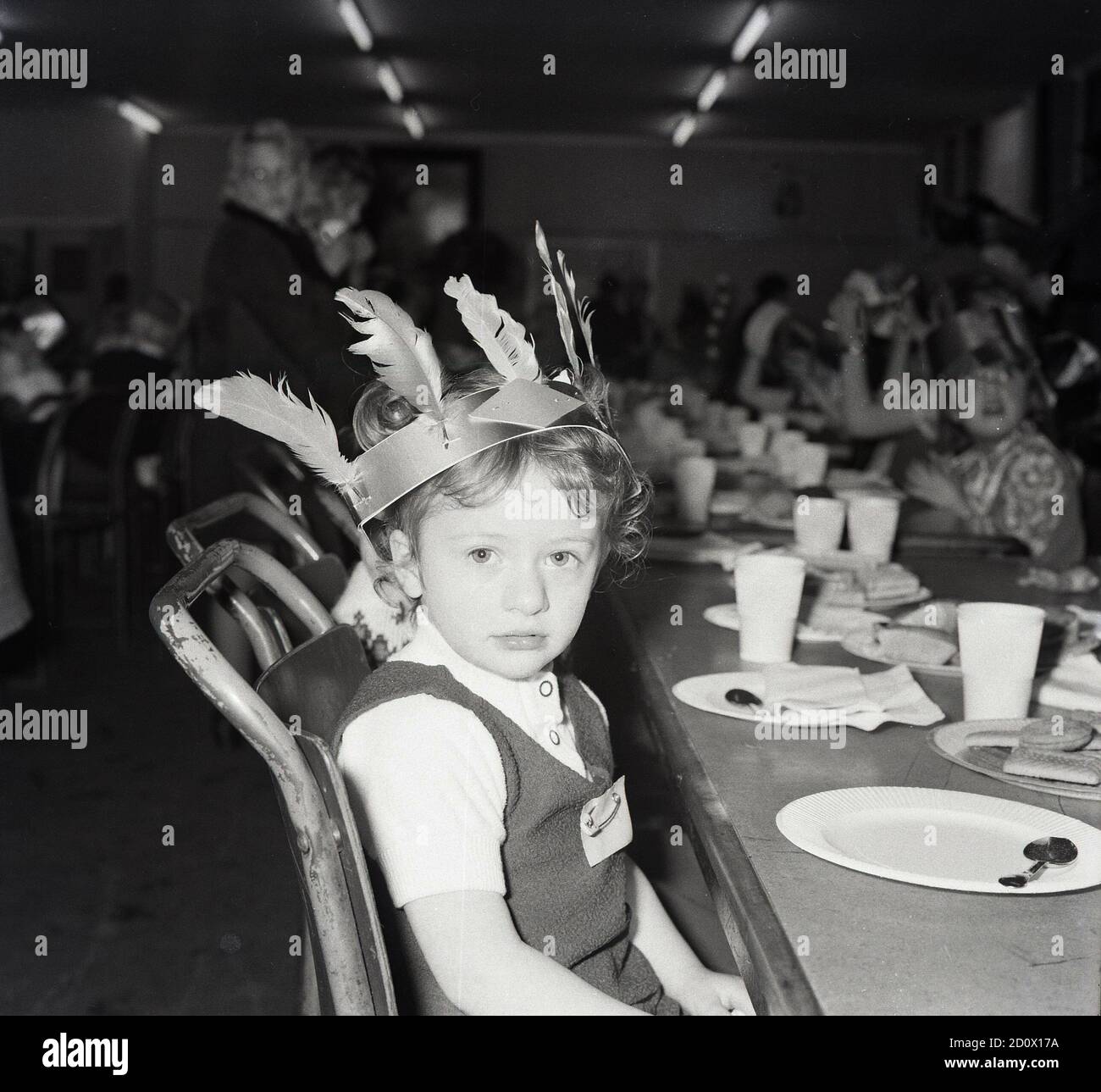 https://c8.alamy.com/comp/2D0X17A/1970s-historical-childrens-party-a-soulful-young-girl-wearing-a-party-hat-indian-style-with-feathers-sitting-at-a-long-table-looking-at-the-camera-england-uk-2D0X17A.jpg