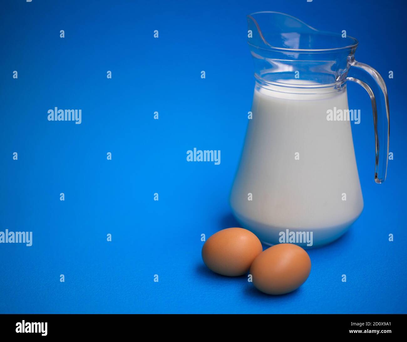 Milk in a glass jug and two eggs on a blue background Stock Photo Alamy