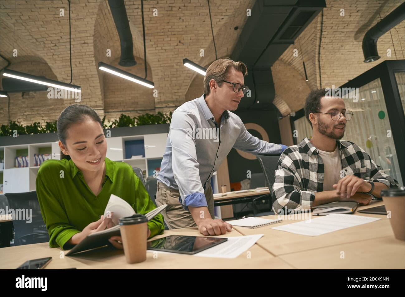 Multicultural business people working on project together in the modern office, confident caucasian male boss or executive communicating and sharing ideas with diverse team. Collaboration and teamwork Stock Photo