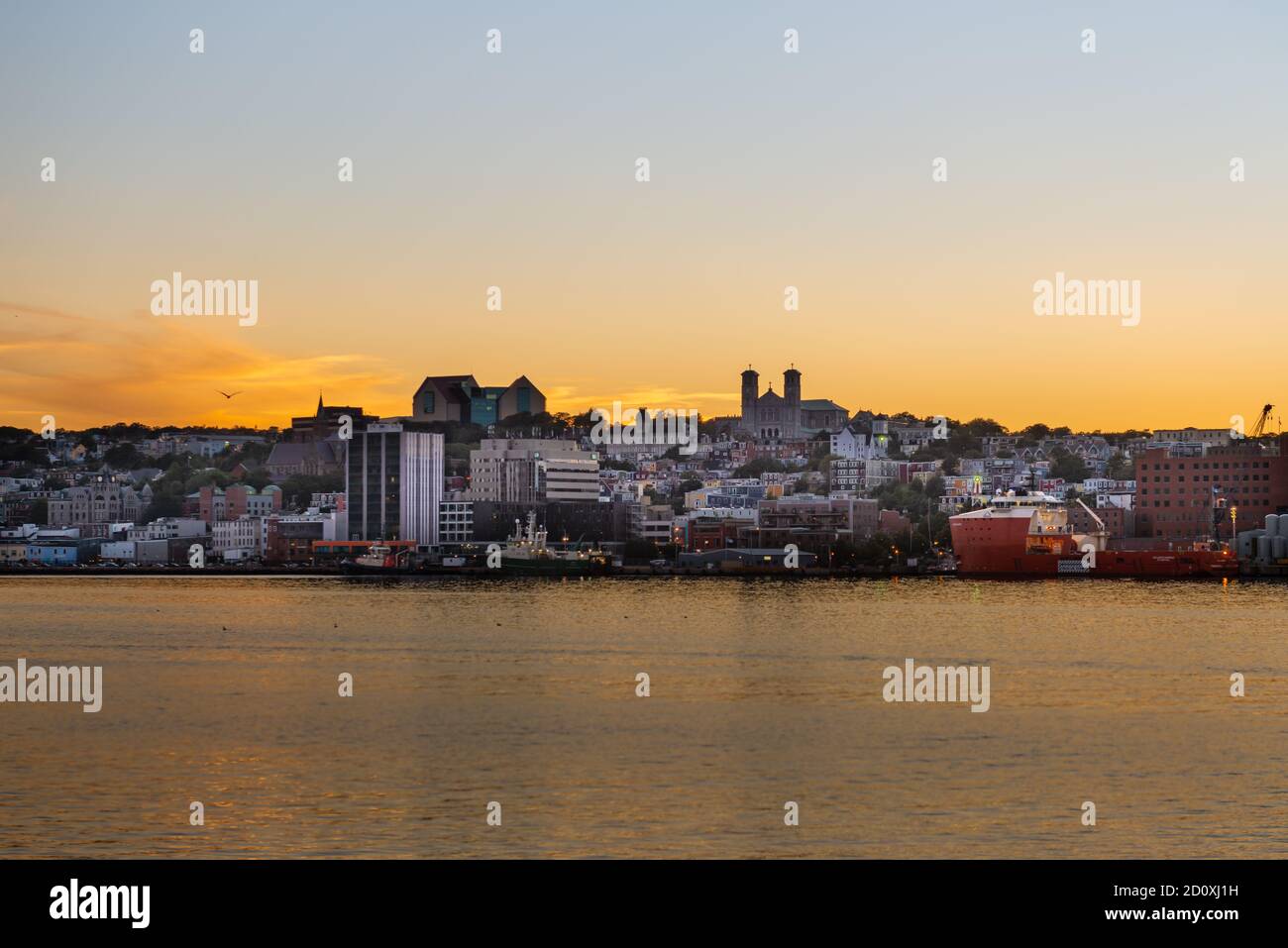 St. John's, Newfoundland, Canada  The sky turns orange as the sun sets behind the downtown area of St. John's with the ocean in the foreground. Stock Photo