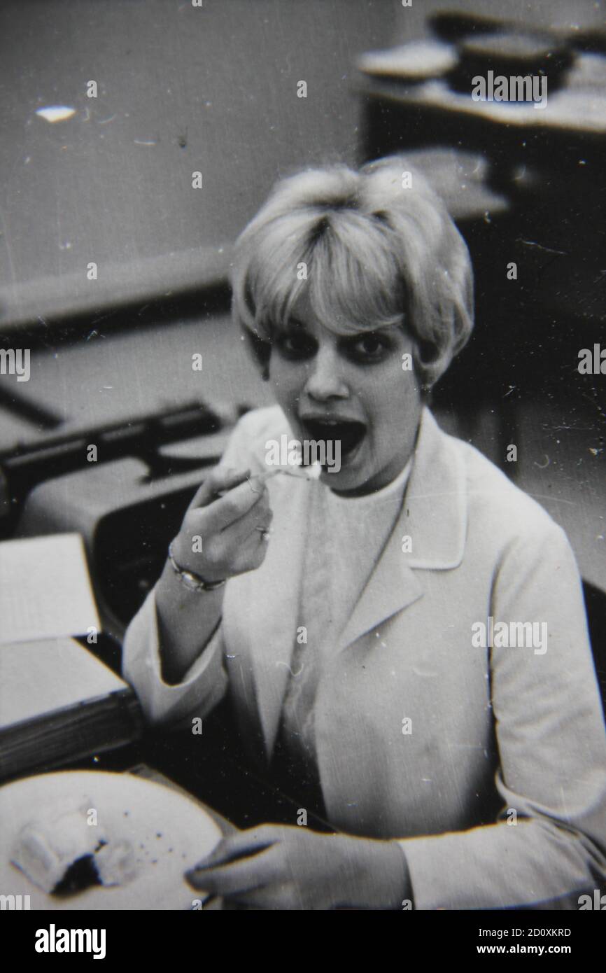 Fine 1970s vintage black and white photography of a young working woman eating in the lunchroom wearing lots of makeup. Stock Photo