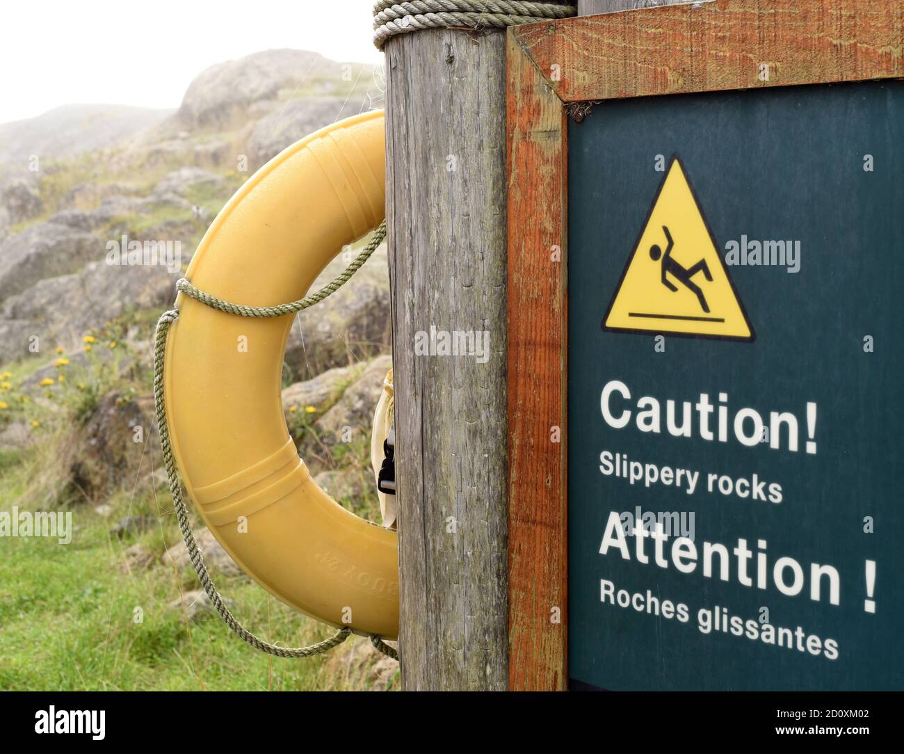 A bilingual Parks Canada (Parcs Canada) sign warning of slippery rocks, roches glissante in French, and life preserver ring at the Fort Rodd Hill and Stock Photo