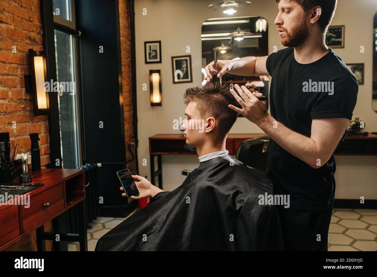 Hardworking hairdresser making a haircut for a young man in a barber shop Stock Photo