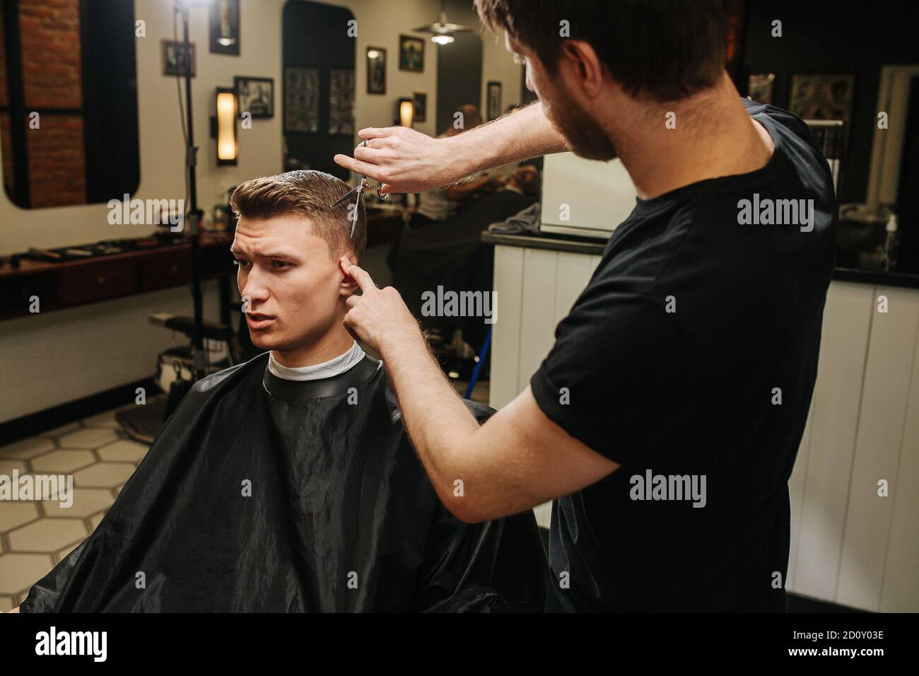 Hairdresser folding ear, making a haircut for a young man in a barber shop Stock Photo