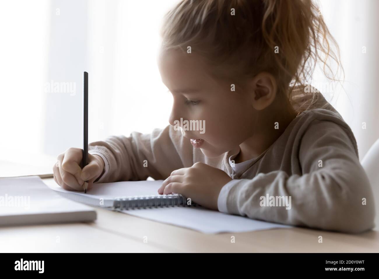 Close up serious little girl writing in notebook, studying Stock Photo