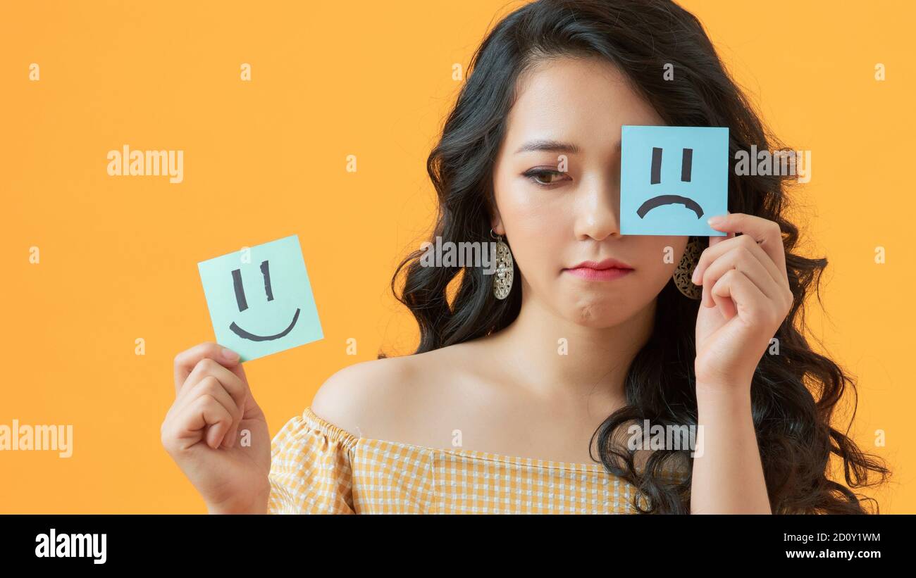 Close-up portrait of attractive girl holding in hands two different emotion stickers isolated on vivid color background Stock Photo