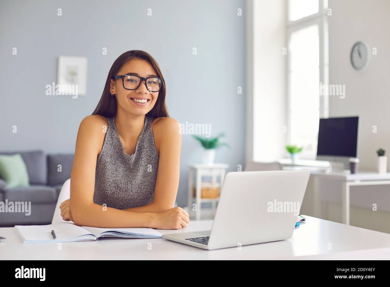 Happy young woman in cool eyeglasses sitting at desk with open laptop and notebook looking at camera Stock Photo