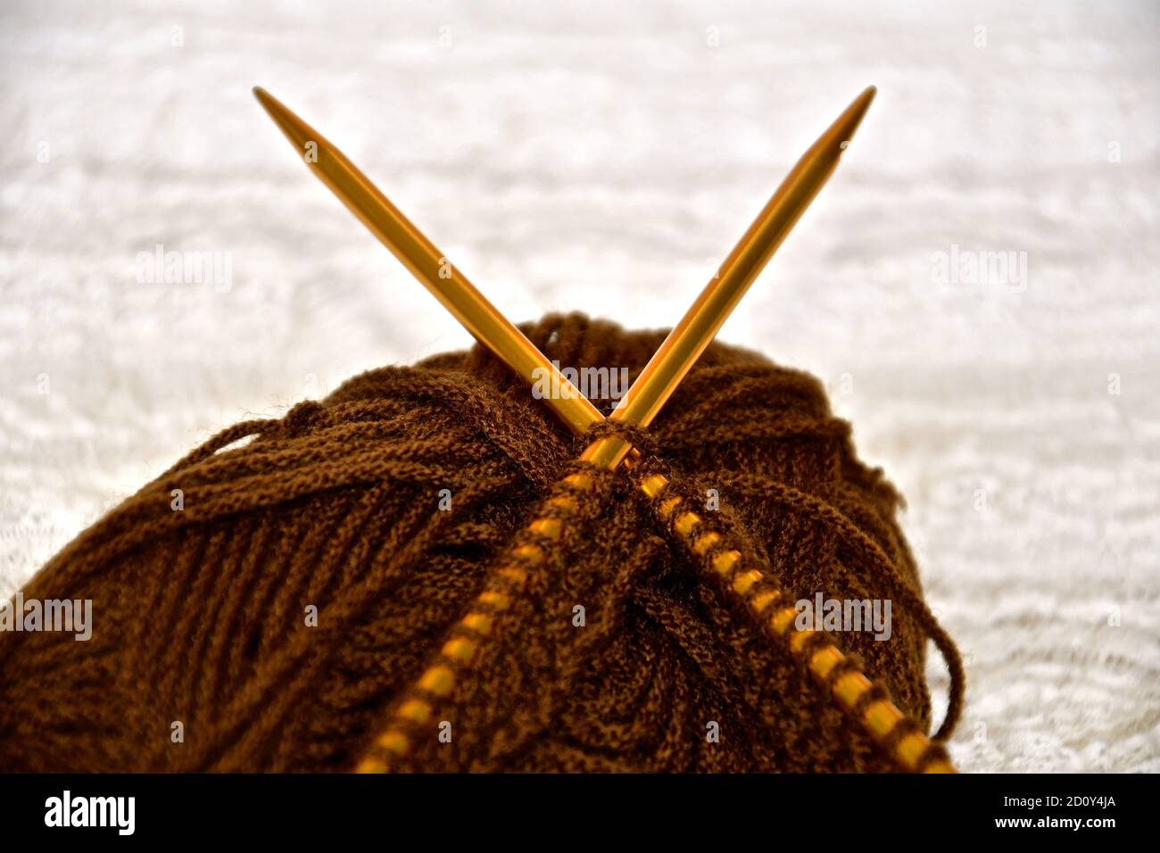 Close up view of knitting and metallic gold knitting needles on a ball of thread with a blurred cream textured background. Stock Photo